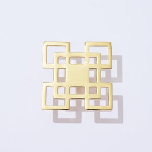 May include: Gold-toned metal geometric design with a square shape and intricate cut-out details. The design features multiple overlapping squares creating a lattice pattern.