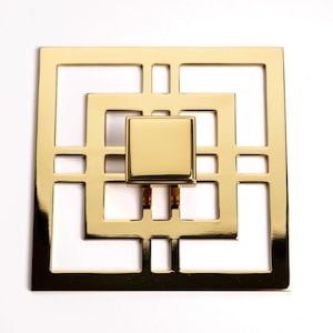 May include: Gold cabinet knob with a square design featuring a geometric pattern. The knob has a square shape and a smooth, polished finish.