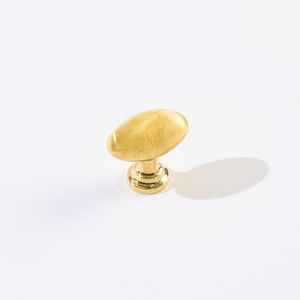 May include: A gold-colored oval cabinet knob with a round base. The knob has a smooth, polished finish and is designed for use on drawers or cabinet doors. The hardware is made of metal and is shown against a white background.