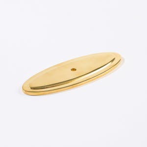 May include: A gold-colored, oval-shaped cabinet pull with a single hole. The hardware has a raised, double-layered design and a polished finish. This decorative piece is suitable for furniture restoration or new construction.