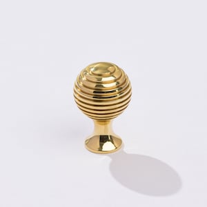 May include: A gold-toned cabinet knob with a round, ribbed design and a short, round base.