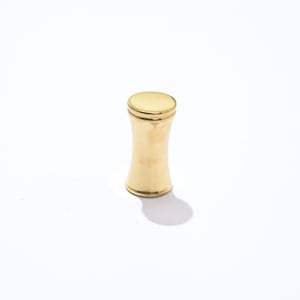 May include: A gold-colored metal knob with a cylindrical shape and a slightly flared top.