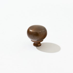 May include: A round, brown, metal cabinet knob with a slightly textured surface.