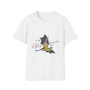 Puede incluir: Camiseta blanca con un gráfico de un dragón negro y dorado con el texto "In my Violence Era" en colores arcoíris.