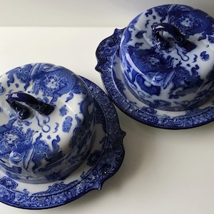 Può includere: Due piatti coperti in porcellana blu e bianca con piatti abbinati. I piatti e i piatti presentano un elaborato motivo a drago e floreale. Ogni piatto ha una maniglia sulla parte superiore. I piatti hanno un bordo smerlato.