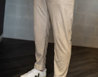 Può includere: Pantaloni in velluto a coste beige con una trama a righe verticali, abbinati a una maglia bianca a maniche lunghe con orlo sfrangiato e sneakers bianche basse con un logo verde scuro sui pannelli laterali.