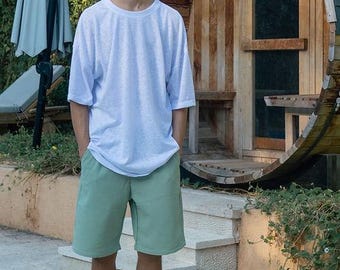 Può includere: Una t-shirt bianca a maniche corte con scollo rotondo e vestibilità ampia, abbinata a pantaloncini color verde salvia che arrivano al ginocchio, caratterizzati da un sottile motivo in tessuto testurizzato. I pantaloncini hanno un taglio dritto.