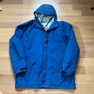 May include: A blue hooded jacket with a full zipper and snap closures. The jacket has two front pockets and adjustable cuffs. The hood has a drawstring. The jacket is made of a waterproof material.