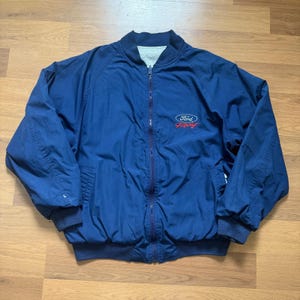 Op de afbeelding: Marineblauwe bomberjack met volledige ritssluiting. Het Ford Racing-logo in rood en wit staat op de borst. Het heeft een geribbelde kraag, manchetten en zoom. De jas is gemaakt van een lichtgewicht materiaal.