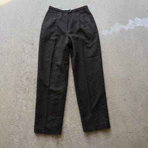 May include: A pair of high-waisted, dark gray trousers with a subtle white grid pattern. The pants have a button and zipper closure, pleats at the waist, and a straight leg design. The fabric appears to be a woven material.