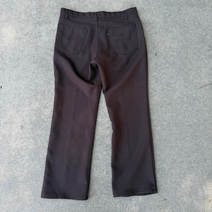 Puede incluir: Pantalones marrones oscuros con dos bolsillos traseros y un bolsillo pequeño en el lado derecho. Los pantalones tienen un diseño de pierna recta y cierre de botón y cremallera. Los pantalones son de tela marrón oscuro lisa.
