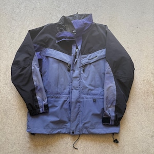 Puede incluir: Chaqueta Moonstone negra, azul y morada. La chaqueta tiene cuello alto, cierre de cremallera y múltiples bolsillos. Las mangas tienen puños ajustables. La chaqueta está diseñada para actividades al aire libre.