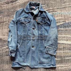 May include: A vintage blue denim jacket with a button-up front, two chest pockets, and two lower pockets. The jacket has a belt detail at the waist and buttoned cuffs. The Levi's logo is visible on the collar.
