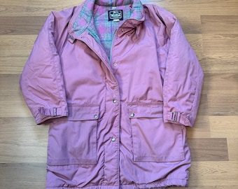 May include: A dusty rose-colored coat with a button-up front, two front pockets, and adjustable sleeve cuffs. The coat features a plaid lining in the collar and a Woolrich logo patch.