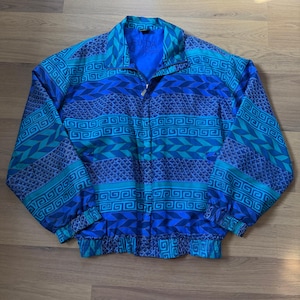 May include: A blue and teal vintage jacket with a geometric pattern. The jacket has a zipper closure and a stand-up collar. The pattern includes Greek key and chevron designs. The text "FUGA" is visible on the collar.