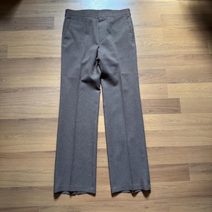Puede incluir: Un pantalón marrón con un diseño de pierna recta. El pantalón tiene cierre de botón y cremallera, trabillas para el cinturón y bolsillos delanteros. La tela parece ser de peso medio.