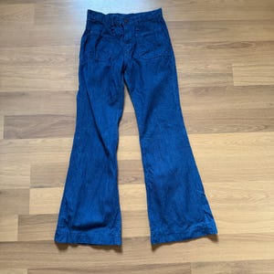 Puede incluir: Pantalones vaqueros azules de campana. Los pantalones tienen cintura alta, dos bolsillos delanteros y cierre de botón y cremallera. Las perneras se ensanchan desde la rodilla hasta el dobladillo. Los pantalones son de tejido vaquero de peso medio.