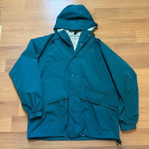 May include: Teal-colored hooded jacket with a full zipper and snap closures. The jacket features two front pockets with zippers and the brand name "L.L.Bean" on the front. The hood has a drawstring, and the jacket has elastic cuffs.