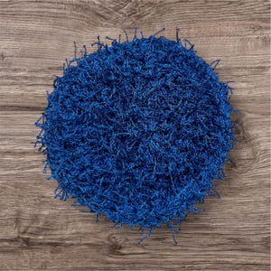 May include: A round, textured, bright blue item, possibly a rug or decorative piece. The item is made of looped yarn, creating a dense, shaggy appearance. The background is a wooden surface.