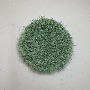 May include: A round, light green, textured scrubby. The scrubby is made of a looped, fibrous material. The object is centered on a light gray background.