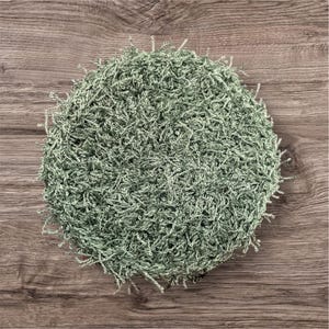 May include: A round, sage green crocheted item with a textured, looped surface. The edges have small, loose fringe. The item is set against a wooden background.