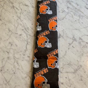 May include: A brown and black fabric heating pad with a repeating pattern of Cleveland Browns football helmets. The fabric has the words "Cleveland Browns" printed on it.