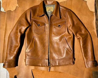 May include: A brown leather jacket with a zipper closure and two flap pockets. The jacket is laid out on a piece of brown leather.
