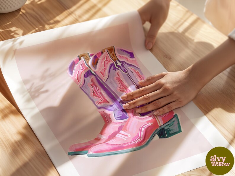 May include: A pair of pink cowboy boots with purple and white floral designs. The boots are painted on a light pink background.