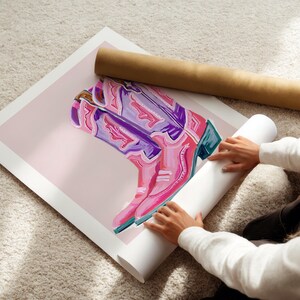 May include: A pink and purple cowboy boot with intricate details is rolled up in a white tube. The boot is on a pink background.