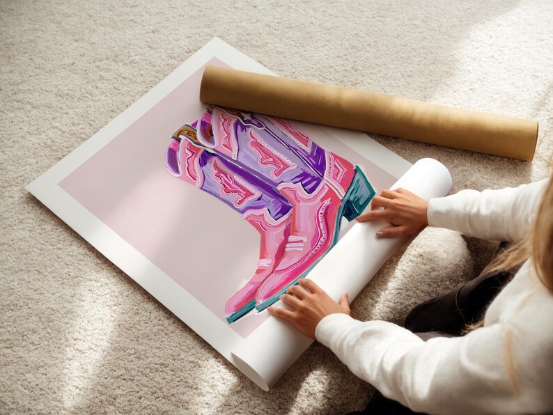 May include: A pink and purple cowboy boot with intricate details is rolled up in a white tube. The boot is on a pink background.