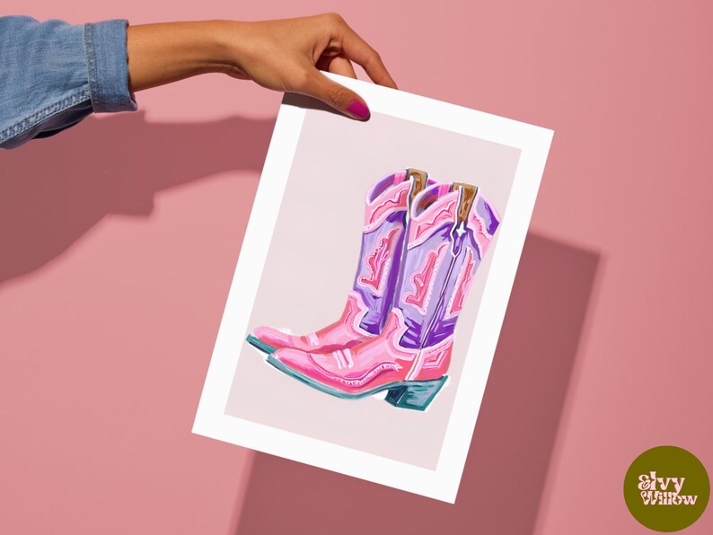 May include: A print of a pair of pink and purple cowboy boots with intricate stitching details. The boots are set against a light pink background.