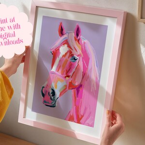 Peut inclure: Une peinture d'une t&ecirc;te de cheval rose sur un fond violet. Le cheval a une bande blanche sur le nez et porte une bride rose. La peinture est encadr&eacute;e dans un cadre rose.