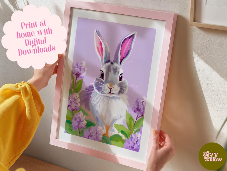 K&ouml;nnte beinhalten: Ein digitaler Druck eines grauen Kaninchens mit rosa Ohren, umgeben von lila Blumen auf einem helllila Hintergrund. Der Druck ist in einem rosa Rahmen gerahmt.