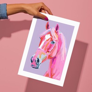 Peut inclure: Une illustration de t&ecirc;te de cheval rose avec une &eacute;toile blanche sur le front, peinte dans un style abstrait et vibrant sur un fond violet clair.