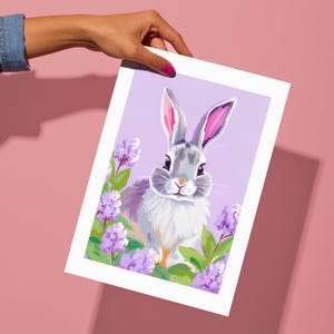 K&ouml;nnte beinhalten: Eine digitale Illustration eines grauen Kaninchens mit rosa Ohren, umgeben von lila Blumen auf einem helllila Hintergrund.
