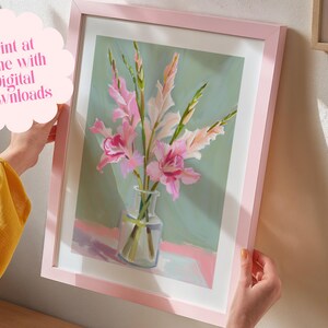 May include: A framed print of a painting of pink gladiolus flowers in a clear glass vase on a light pink surface. The background is a light green colour. The frame is pink.