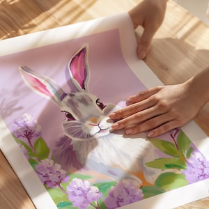 K&ouml;nnte beinhalten: Ein graues Kaninchen mit rosa Ohren sitzt in einem Feld mit lila Blumen. Das Kaninchen schaut den Betrachter mit einem s&uuml;&szlig;en Ausdruck an. Der Hintergrund ist in einem zarten Lila gehalten.