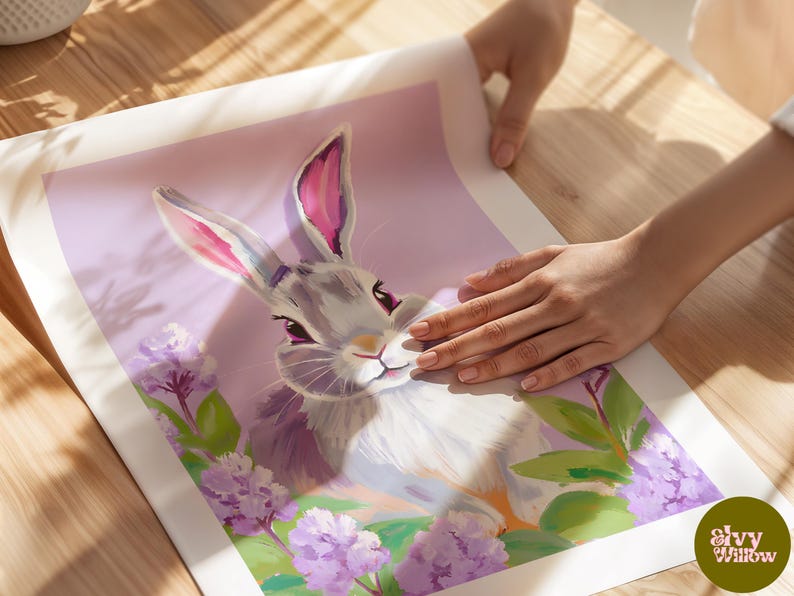 K&ouml;nnte beinhalten: Ein graues Kaninchen mit rosa Ohren sitzt in einem Feld mit lila Blumen. Das Kaninchen schaut den Betrachter mit einem s&uuml;&szlig;en Ausdruck an. Der Hintergrund ist in einem zarten Lila gehalten.