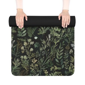 May include: A black yoga mat with a green and white floral pattern. The mat is rolled up and being held by two hands.