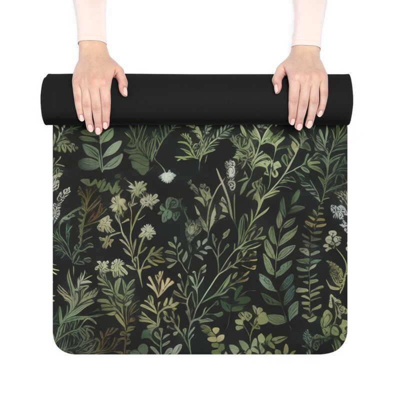 May include: A black yoga mat with a green and white floral pattern. The mat is rolled up and being held by two hands.