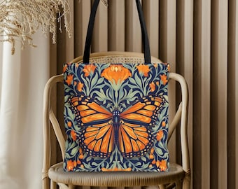 May include: A tote bag with a butterfly design. The bag features a large orange and black butterfly on a navy blue background with orange flowers and green leaves. It has black handles and is sitting on a wicker chair.