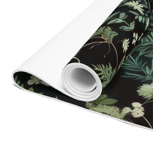 May include: A rolled up yoga mat with a black background and a green and white floral pattern.
