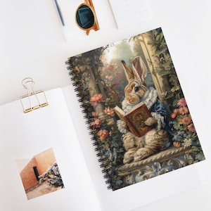 May include: A brown rabbit wearing a blue jacket with a white collar sits on a stone ledge in a garden setting. The rabbit is holding an open book with a red cover and gold accents. The garden is filled with colorful flowers and greenery.
