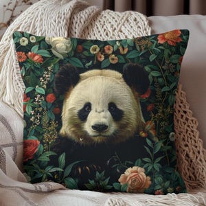 May include: A black and white panda bear peeking out from behind lush green foliage with pink and white flowers. The panda has black eyes and a black nose. The background is a dark green.
