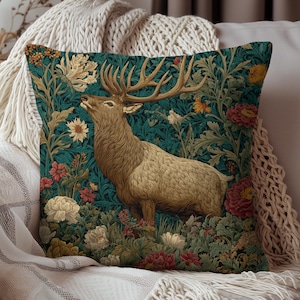 May include: Decorative square pillow featuring a detailed illustration of a majestic elk amidst a floral tapestry of red, yellow, and white flowers against a teal background. The pillow is a home decor item.