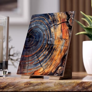 May include: A wooden decorative panel featuring a detailed cross-section of a tree trunk. The image showcases concentric rings in shades of blue, orange, and brown, mounted on a wooden stand. The panel is displayed on a textured surface.