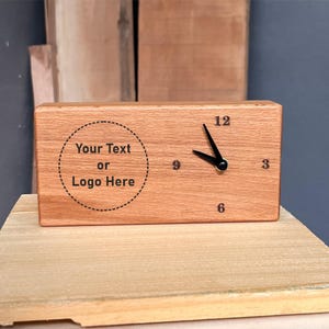 May include: A rectangular wooden clock with black hands and numerals. The clock face has the numbers 3, 6, 9, and 12. The left side of the clock has a circular area with the text "Your Text or Logo Here".