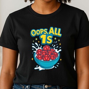 May include: Black t-shirt with the text "OOPS ALL 1S" above a blue bowl filled with red spheres. The design includes yellow stars and white splashes, creating a playful graphic.