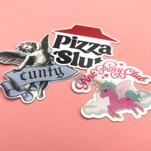 May include: A collection of stickers on a pink background. The stickers include a cherub with the word "c**ty" on a banner, a "Pizza Slut" logo, and a pink unicorn with "Pink Pony Club" text.