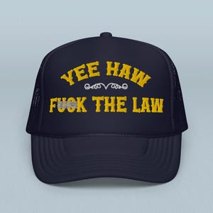 Może przedstawiać: Granatowa czapka typu trucker z haftowanym żółtym napisem "YEE HAW FUCK THE LAW". Czapka ma siatkową tylną część i zakrzywiony daszek, odpowiednia do aktywności na świeżym powietrzu.